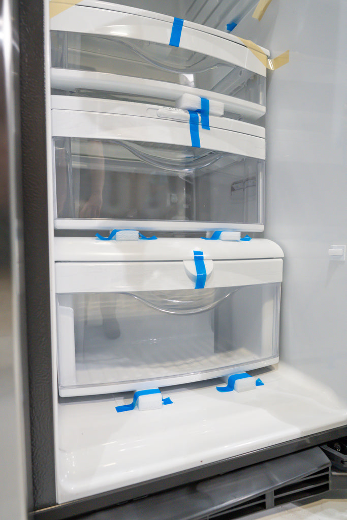 GE GSS25IYN Empty refrigerator with shelves and drawers taped shut, likely for cleaning or moving.