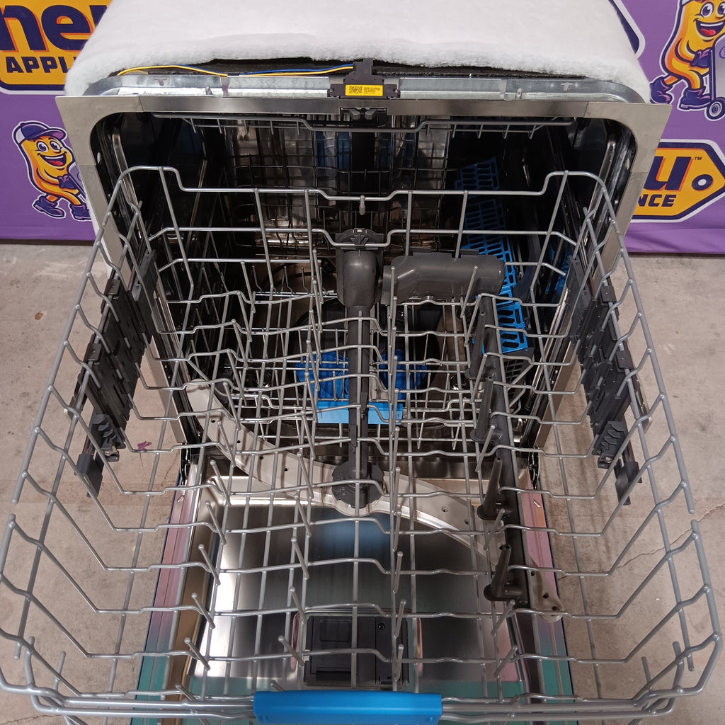 GE PDT715SYVFS Open dishwasher with silverware and dishes inside, on a concrete floor.