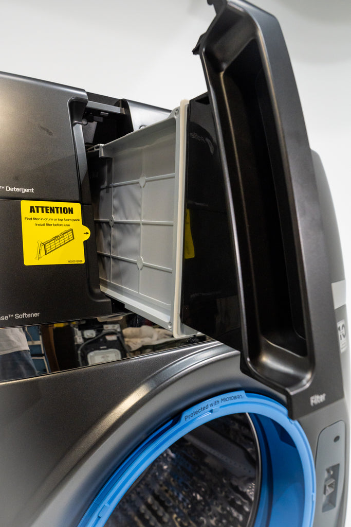 GE Profile PFQ97HSPVDS Open washing machine with a yellow 'Attention' label on a white background